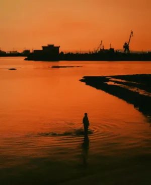 Silhouette Of A Person Walking In Water At Sunset